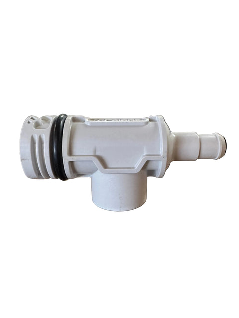 A white plastic plumbing fitting or connector with black rubber O-rings, shown on a brown workbench inside a workshop or shop environment.